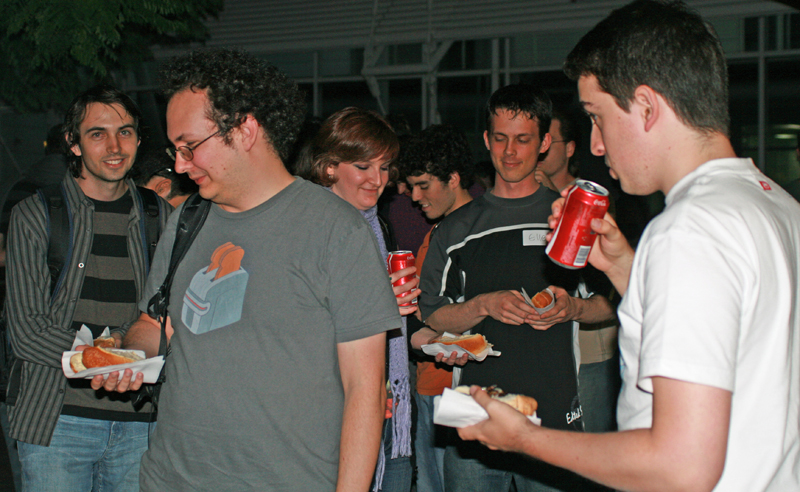 Image of several people drinking coke and eating hot dogs in the evening.