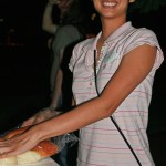 A lady smiling at the camera while taking a hot dog bun out of a bag.