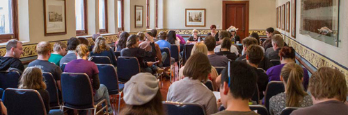 Banner: A roof people sit, watching a panel talk.