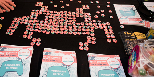 A table at the Perth Games Festivals, covered in themed badges that form the shape of an 8-Bit 'Space Invader'