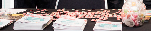 An image of a table, with festival programs, badges, and a jar of lollies.
