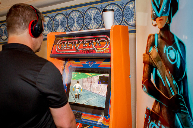 A man wearing headphones plays games on a custom-built arcade machine.